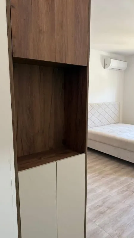 Pogled na drveni ormar u spavaćoj sobi sa krevetom u pozadini.
