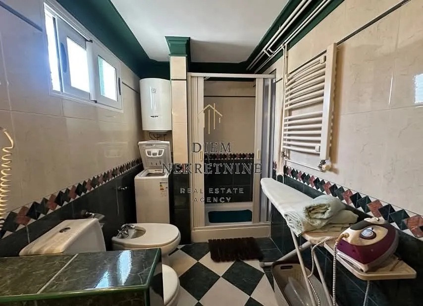Cluttered bathroom with a shower cabin, washing machine, and sanitary fixtures.
