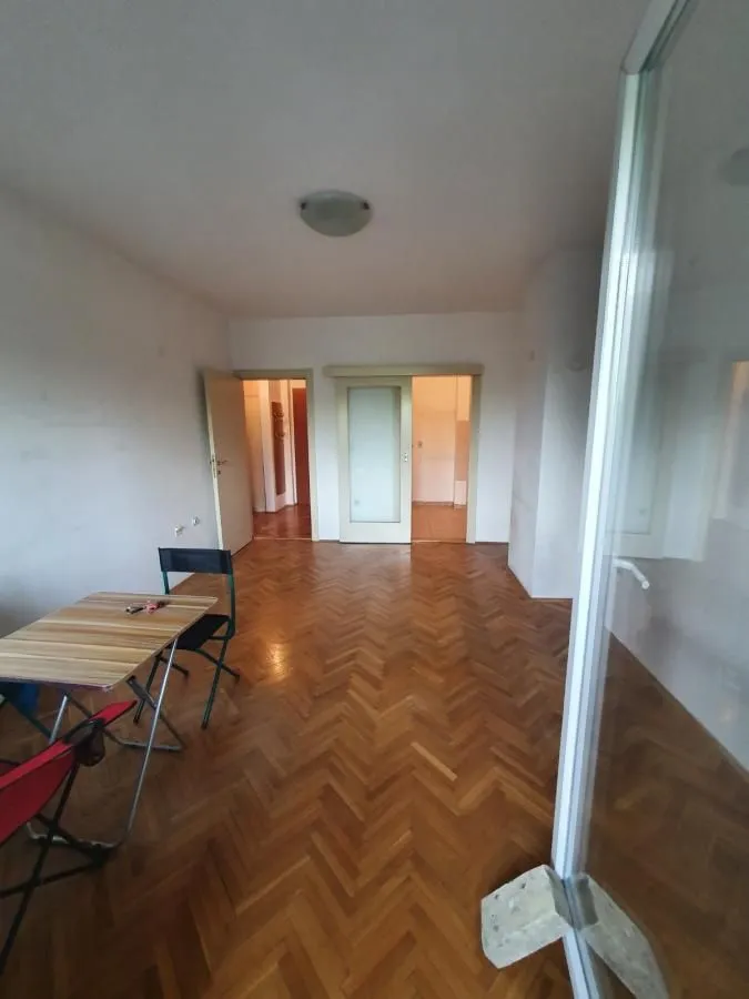 Prazna soba sa drvenim parketom i trpezarijskim stolom.