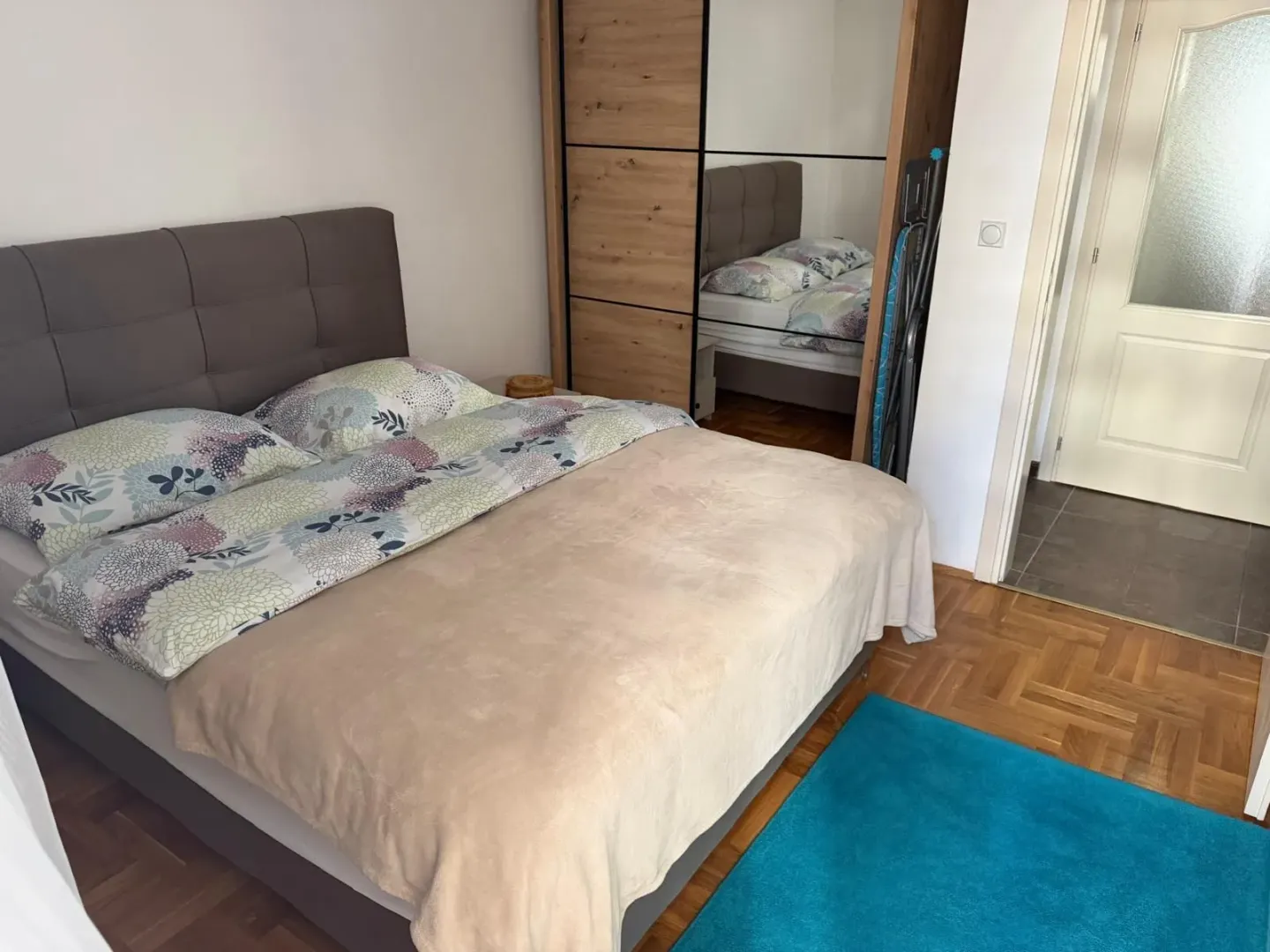 Namještena spavaća soba sa bračnim krevetom, plakarom i parketom.