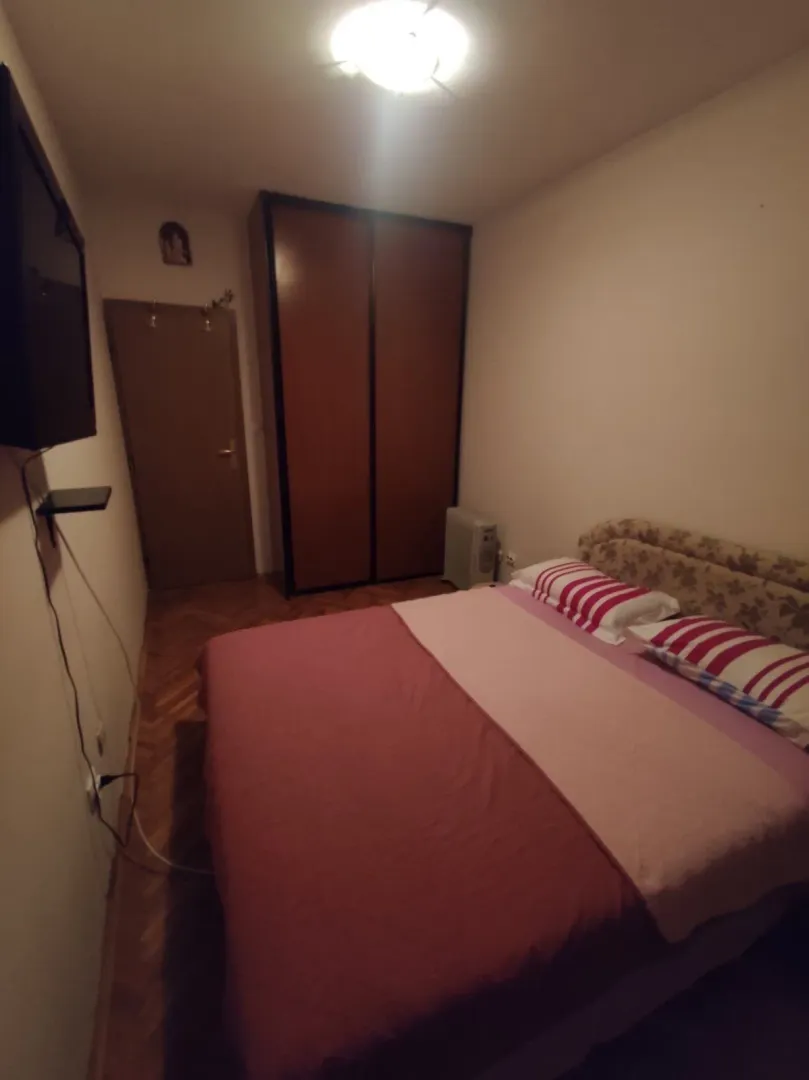 Jednostavna spavaća soba sa bračnim krevetom i drvenim ormarom.
