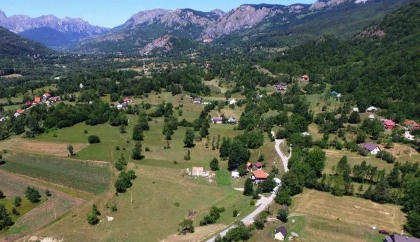 Pogled iz vazduha na prirodu, kuće i zelene površine.