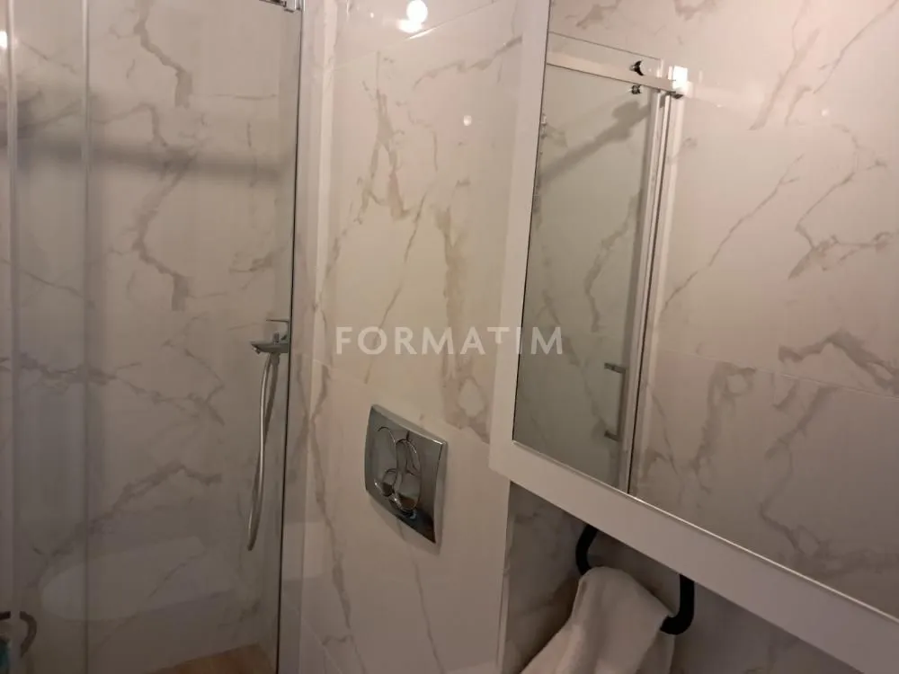 View of the bathroom with a glass shower enclosure and marble-look tiles.