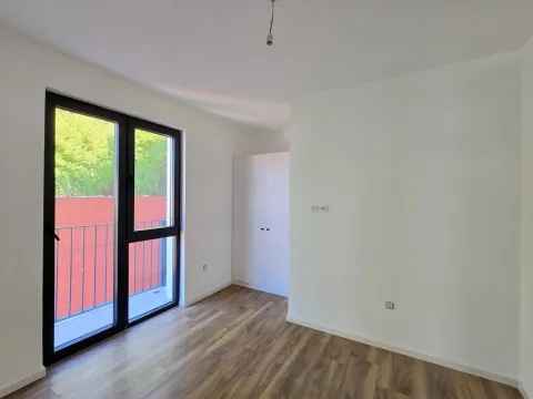 Prazna soba sa bijelim zidovima, drvenim podom i izlazom na balkon. - image 8