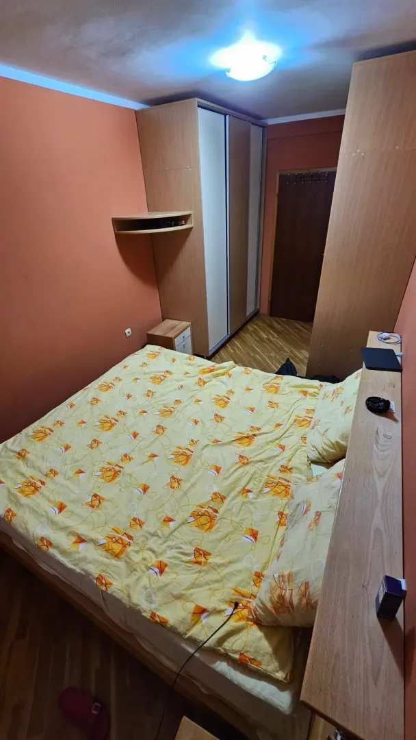 Namještena spavaća soba sa bračnim krevetom, garderoberom i narandžastim zidovima.