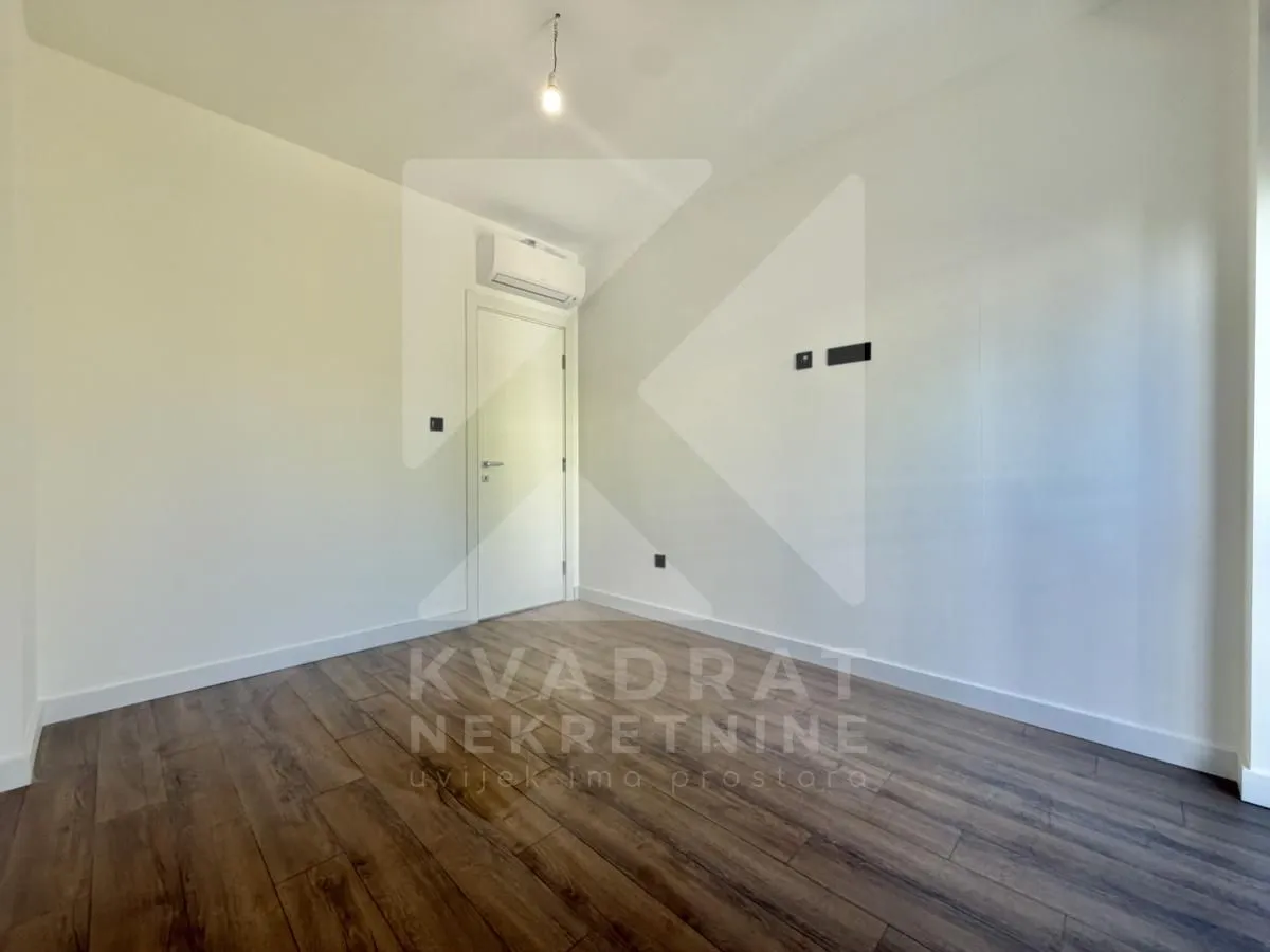 Empty room with white walls, wooden flooring, and an air conditioning unit above the door.