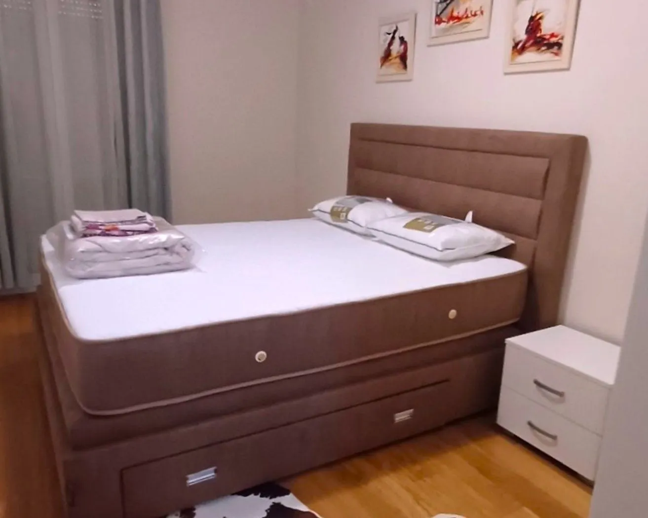 Spavaća soba sa bračnim krevetom, noćnim stočićem i slikama na zidu.