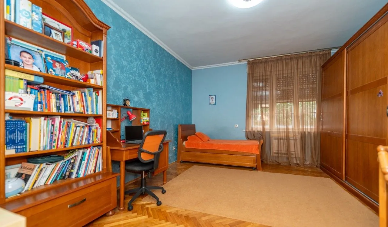Children's bedroom with a bed, desk, large bookcase, and wardrobe.