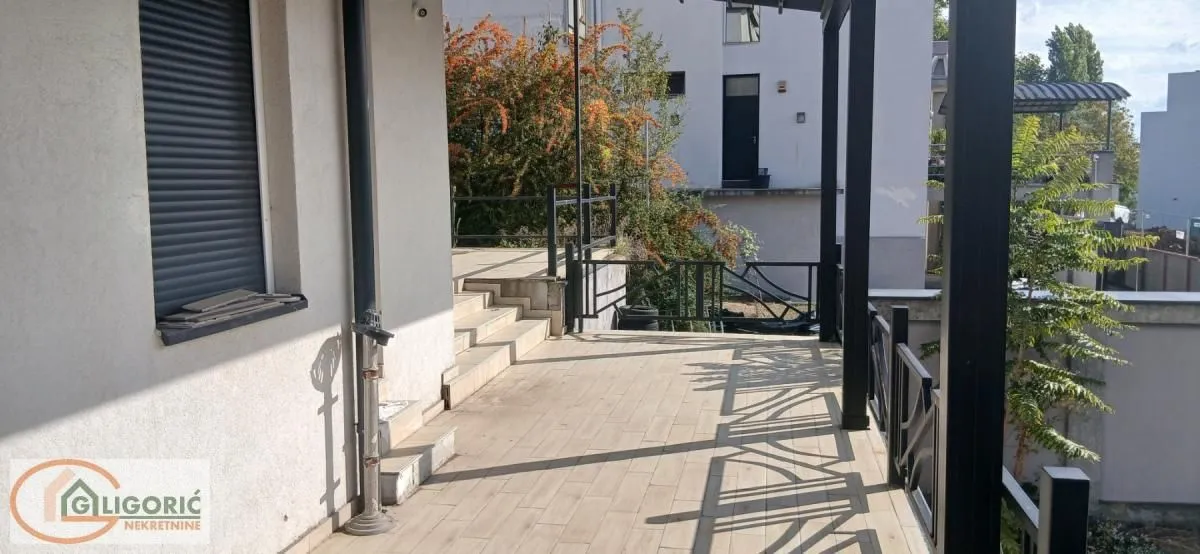 Prostrana popločana terasa sa ogradom ispred ulaza u objekat.