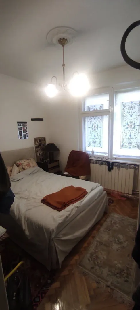 Spavaća soba sa bračnim krevetom, lusterom i prozorima sa vitražom.