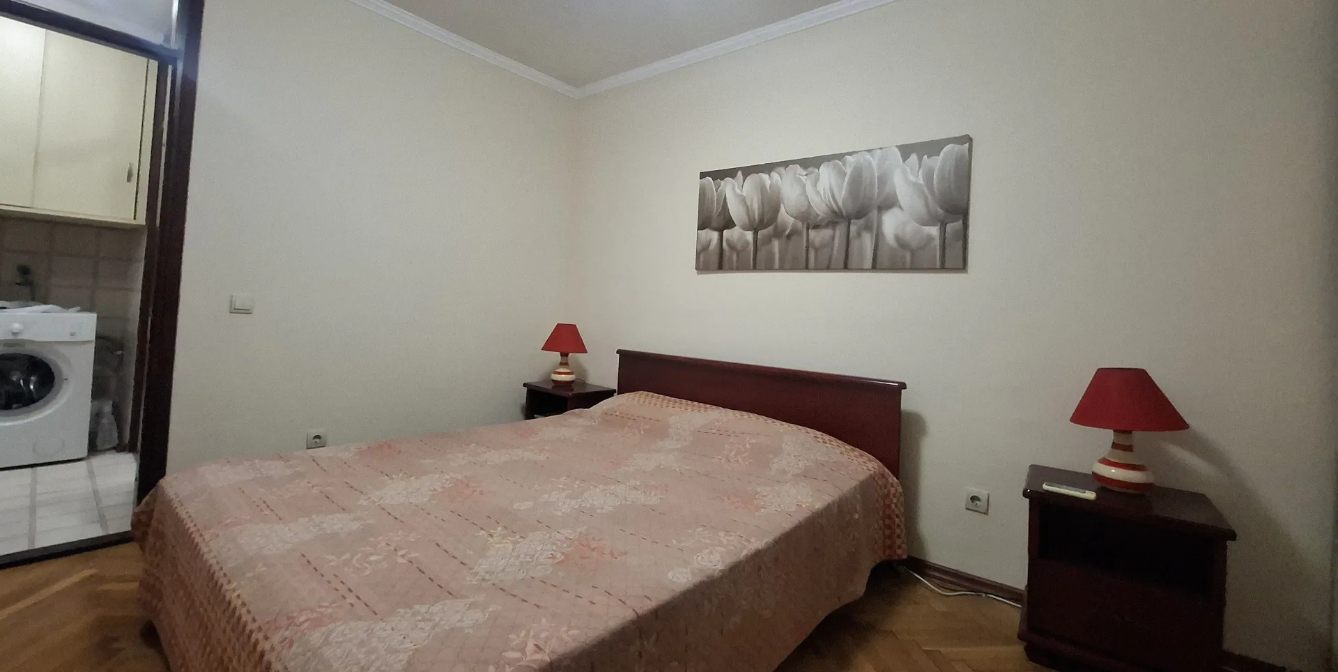 Spavaća soba sa bračnim krevetom, noćnim stočićima i slikom na zidu.