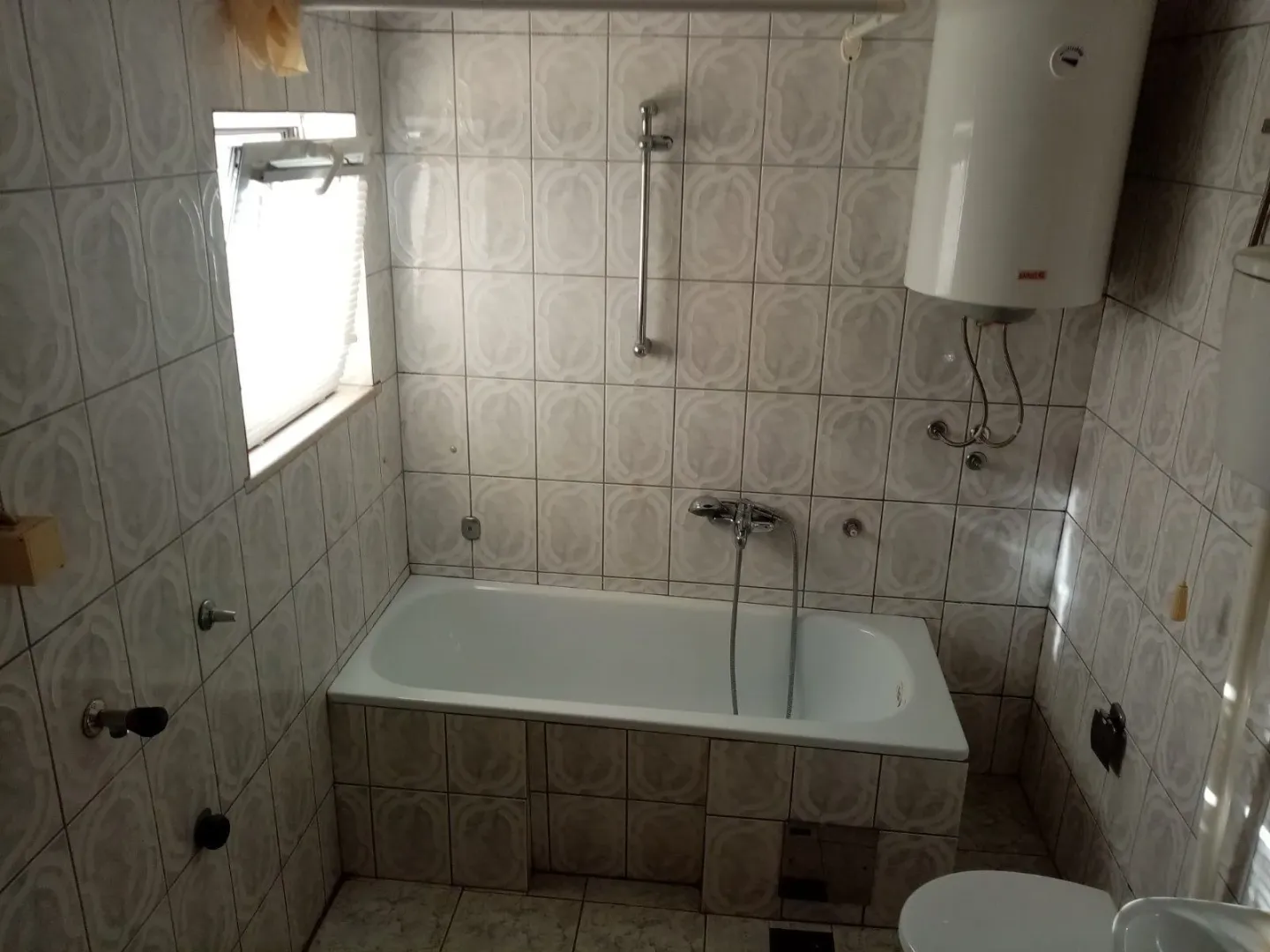 A simple bathroom featuring a bathtub, light tiling, and a water heater.