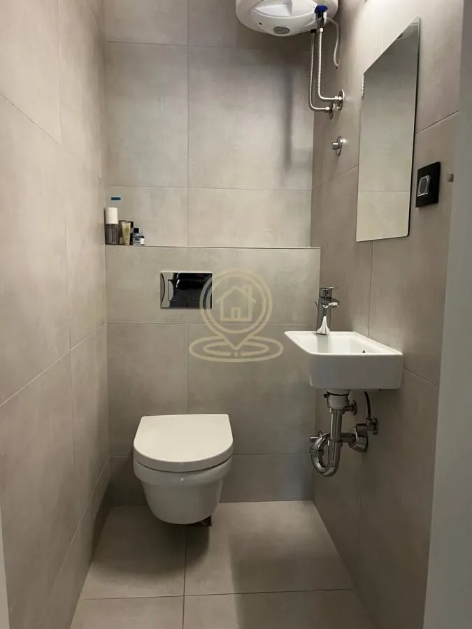 Manje kupatilo sa pločicama u neutralnim tonovima, wc šoljom i umivaonikom.