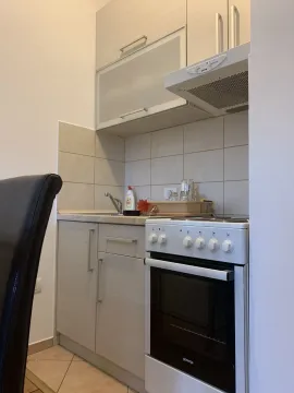 A small kitchen with light cabinets and an electric stove. - image 10
