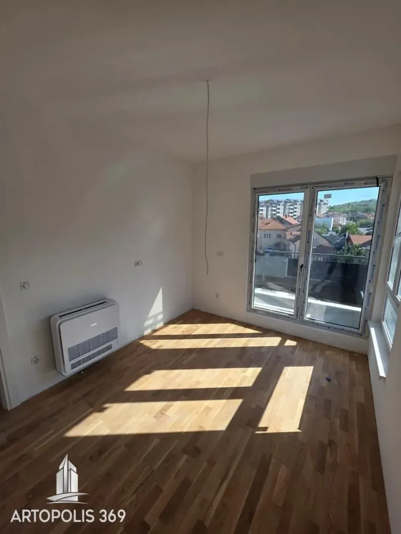 Empty room with wooden flooring, air conditioning unit, and balcony doors.