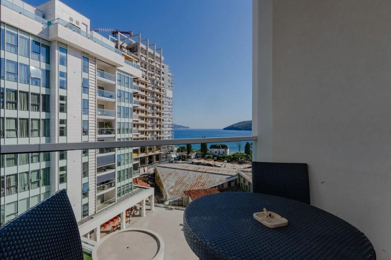 Furnished balcony with seating and a view of the sea and surrounding buildings.