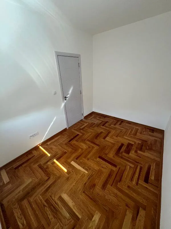 Prazna soba sa belim zidovima i drvenim parketom.