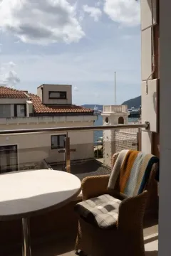 Namješten balkon sa stolom i foteljom i pogledom na more i okolne zgrade. - image 9