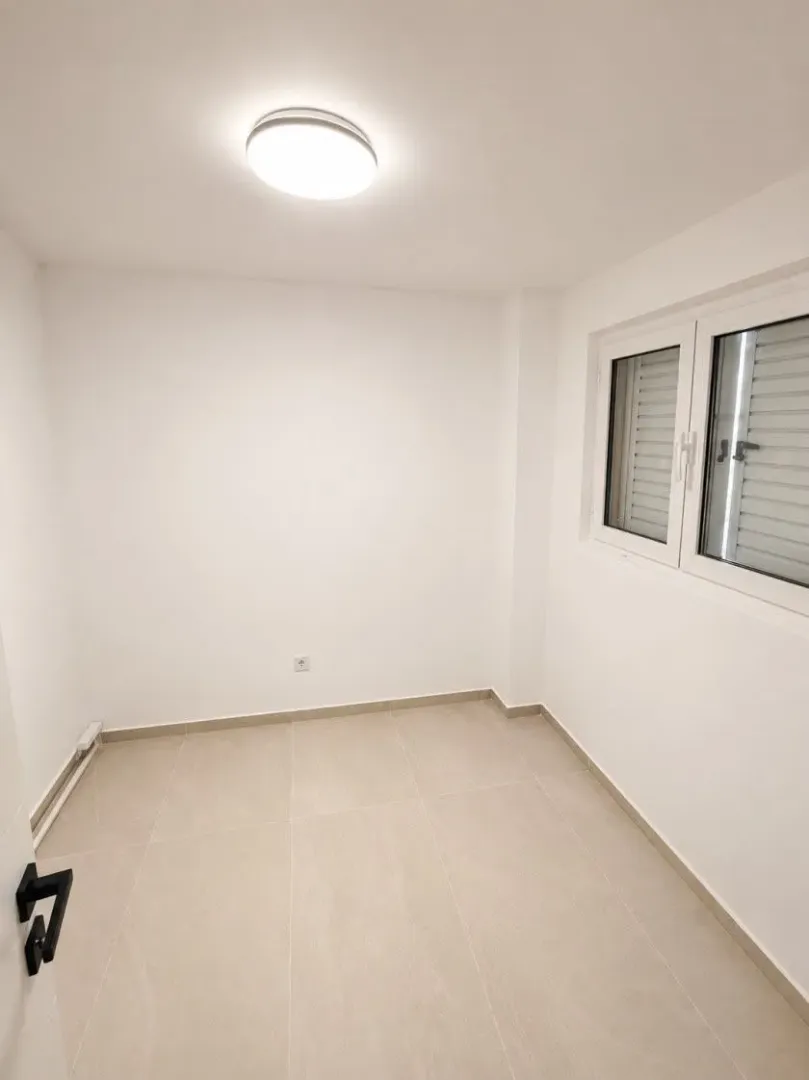 Prazna svijetla soba sa keramičkim pločicama na podu i prozorom.