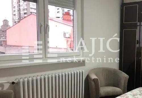Deo spavaće sobe sa foteljom, prozorom i radijatorom.