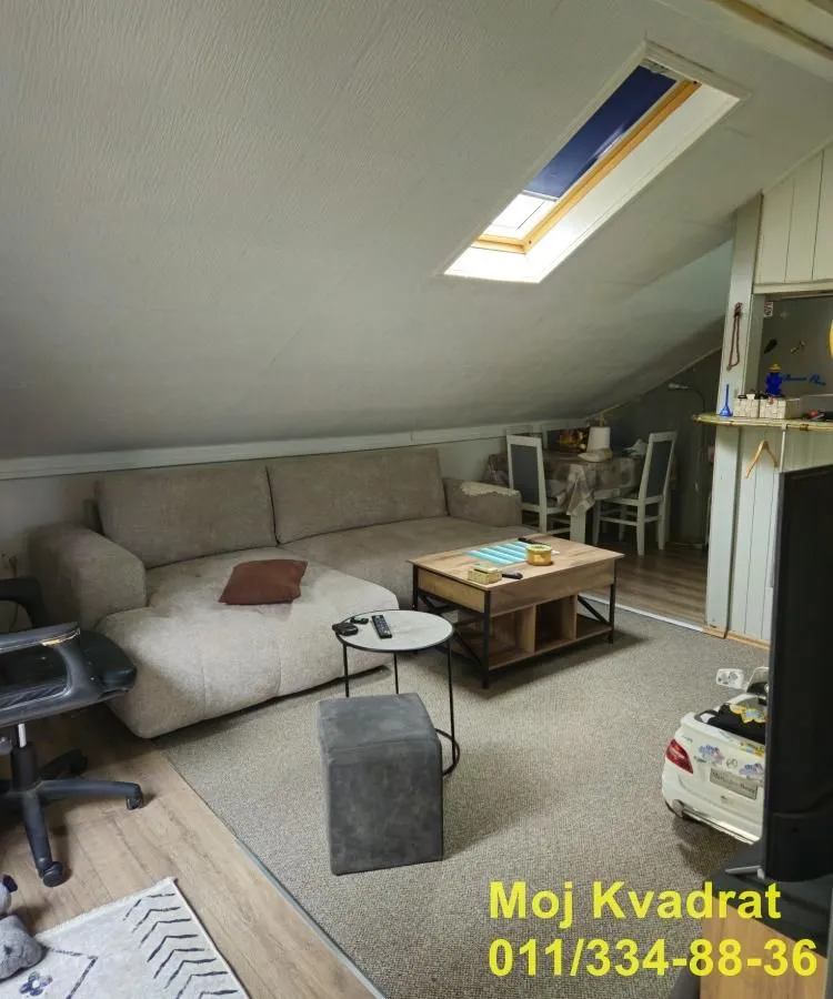 Potkrovlje opremljeno kao dnevna soba sa ugaonom garniturom i krovnim prozorom.