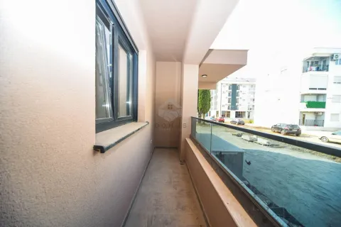 Natkriveni balkon sa staklenom ogradom i pogledom na okolne zgrade i parking. - image 10
