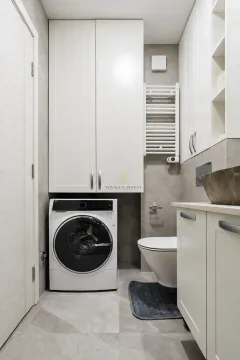 Modern bathroom equipped with a washing machine and built-in cabinetry. - image 10