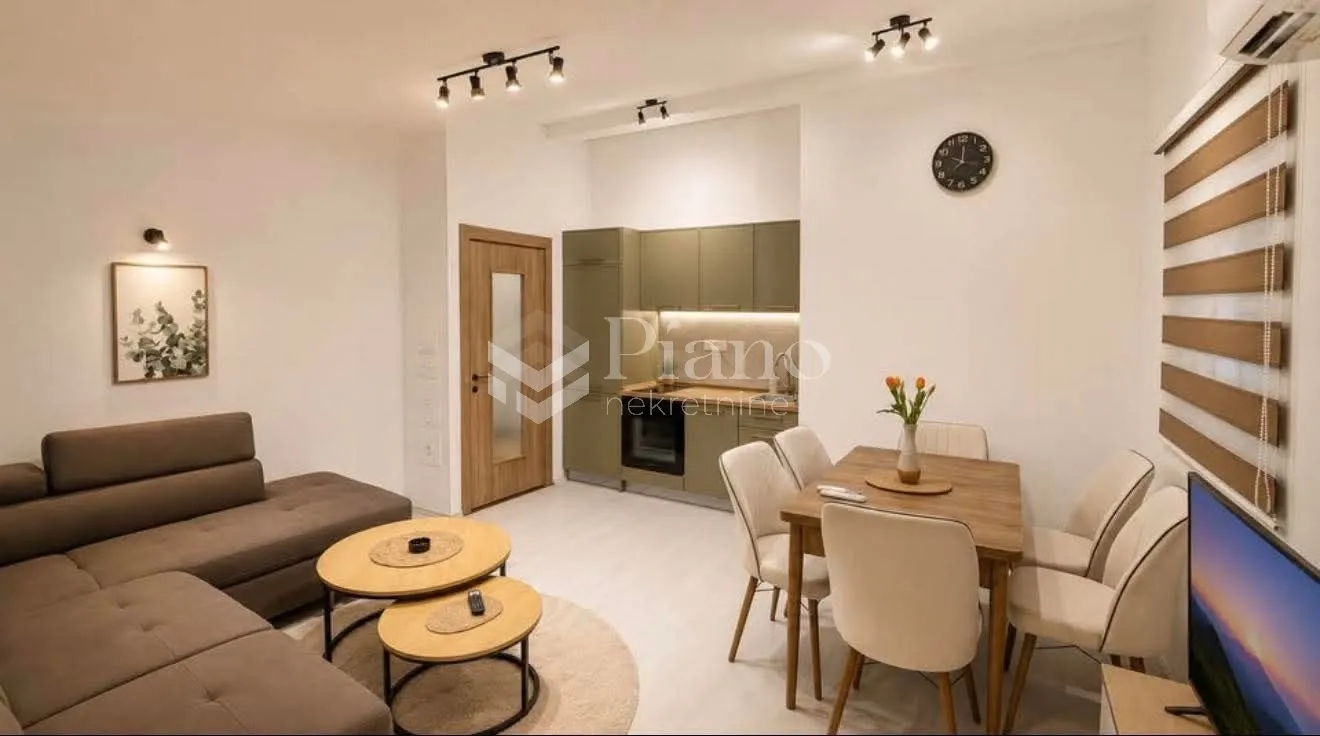 Living room with a sofa set, dining area, and fitted kitchen in the background.