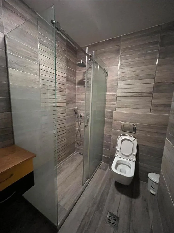 Moderno kupatilo sa tuš kabinom i pločicama u dezenu drveta.