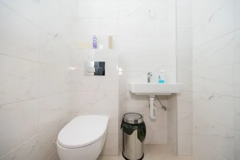 A small toilet room with white tiles, a wall-hung toilet, and a sink. - image 9