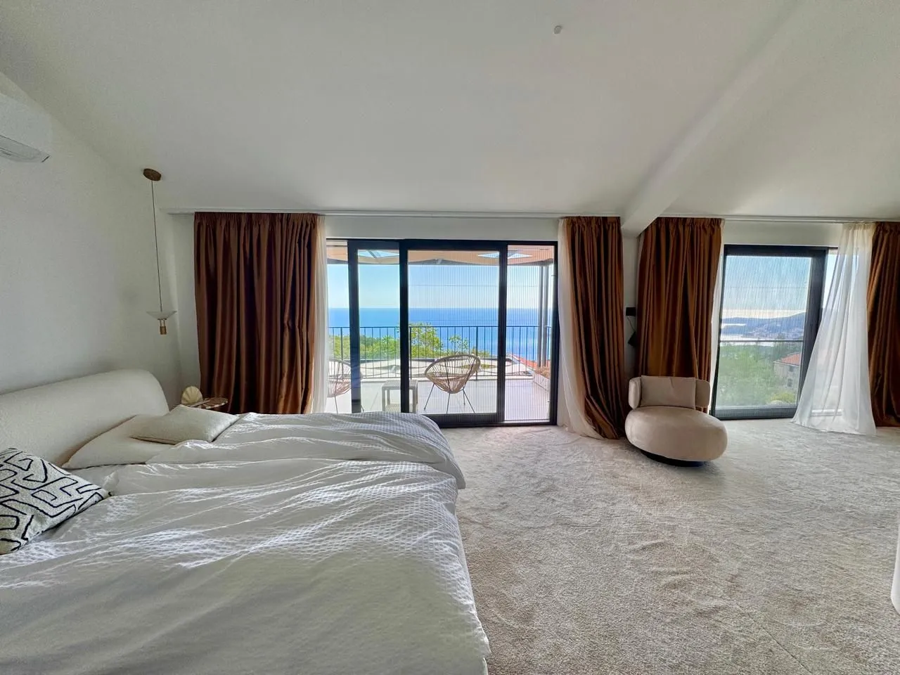 Spacious bedroom with a double bed, carpet, and large glass surfaces with a sea view.