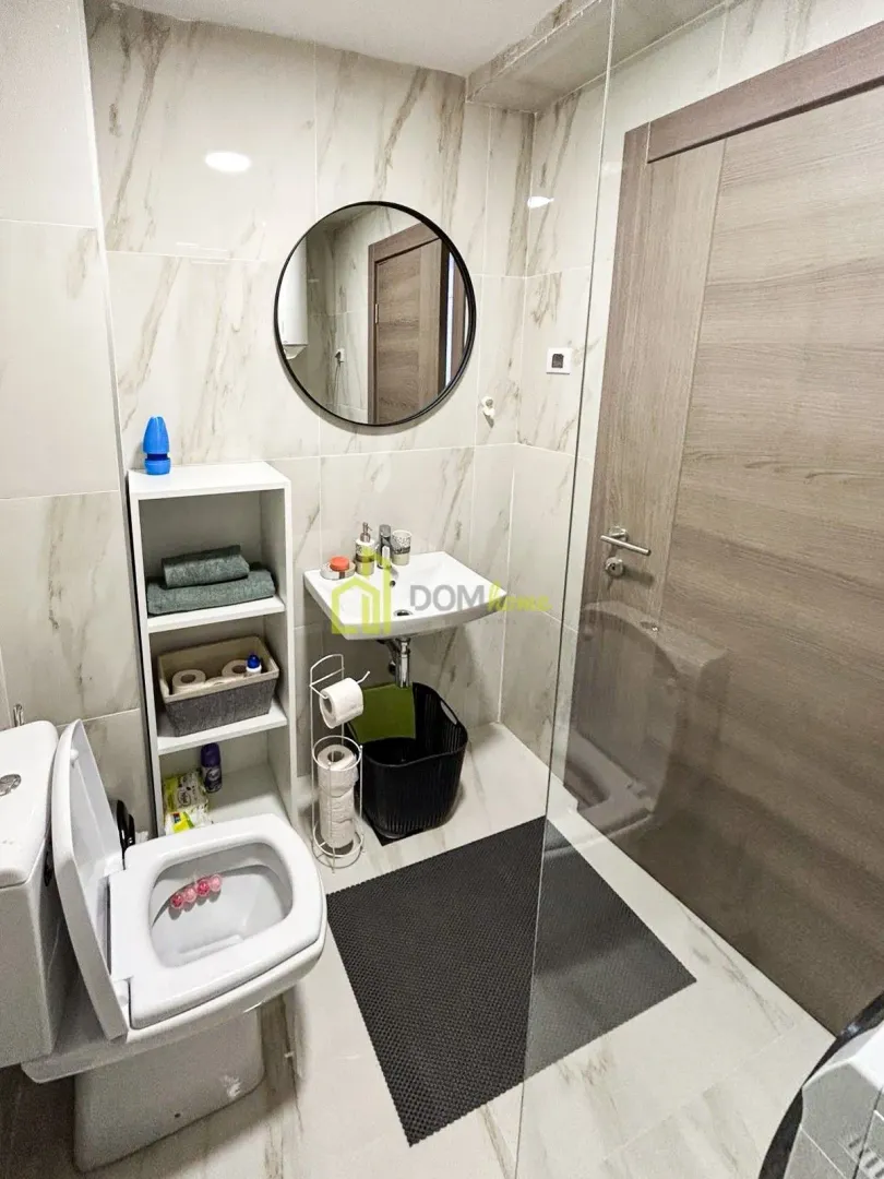 Modern bathroom with a sink, mirror, shelving unit, and toilet.