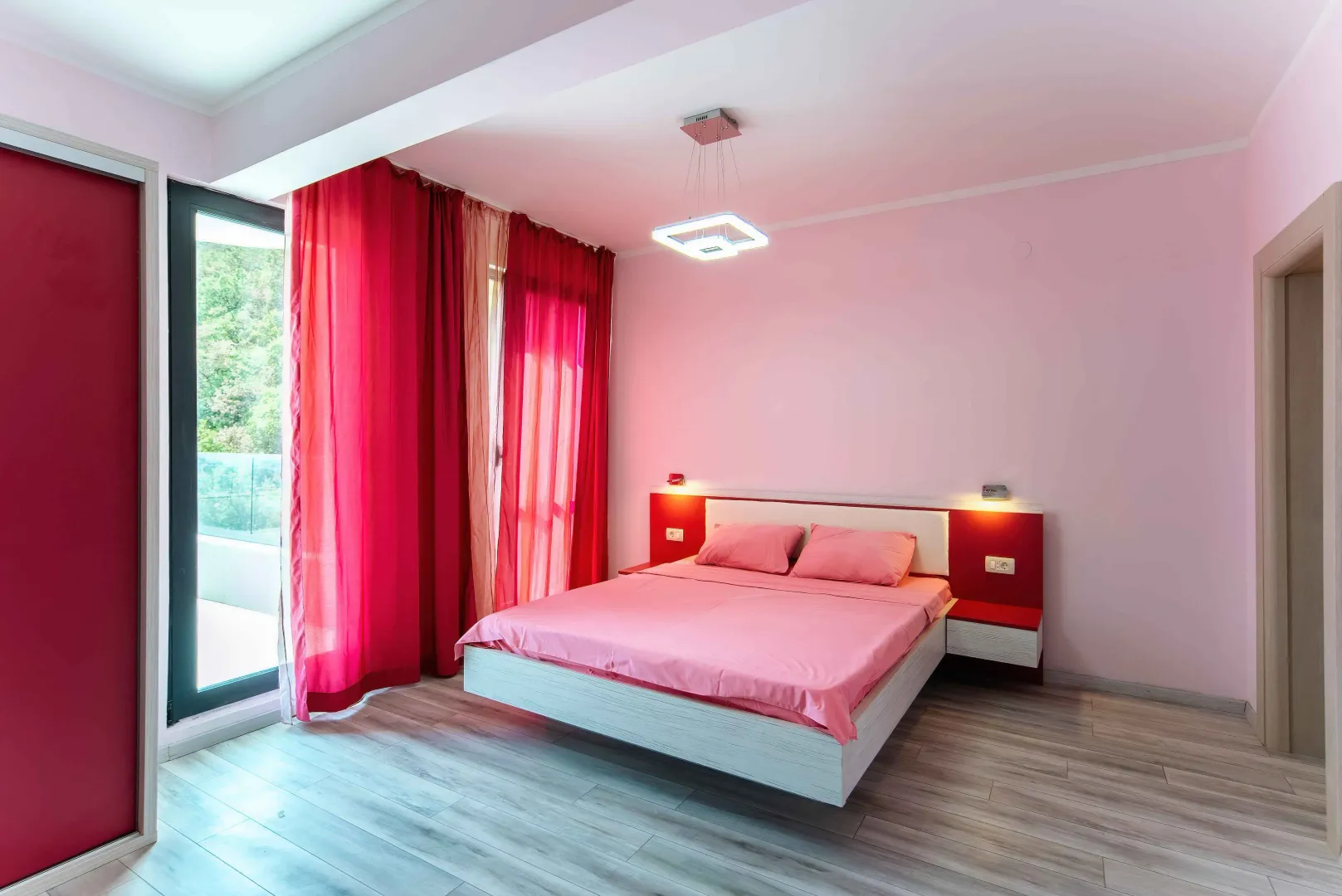 Prostrana spavaća soba sa bračnim krevetom, roze posteljinom i izlazom na terasu.