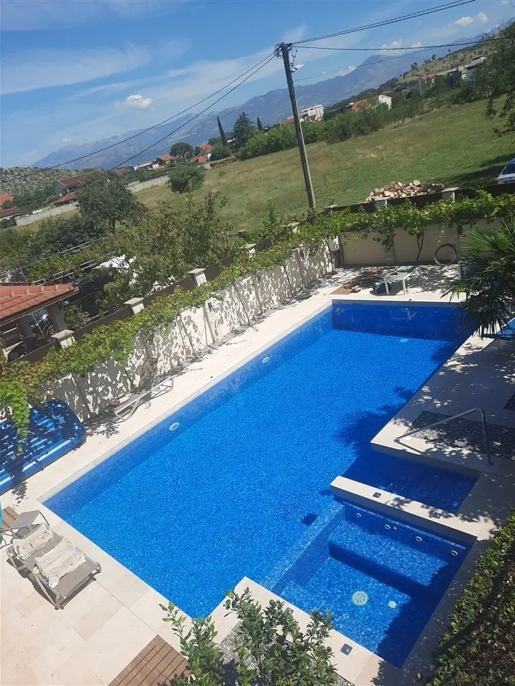 A large outdoor swimming pool in a yard with sun loungers and nature views.