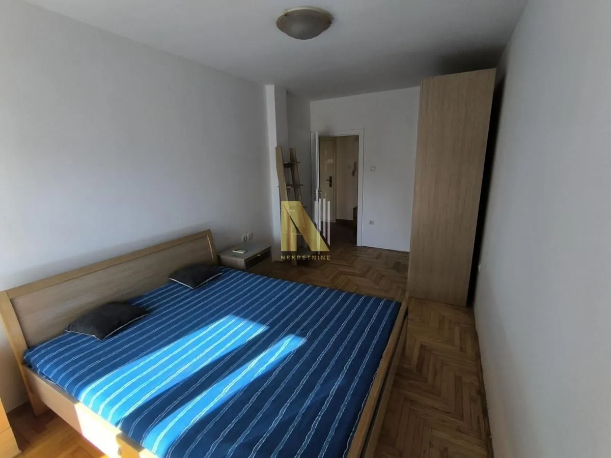 Spavaća soba sa bračnim krevetom, drvenim podom i ormarom.