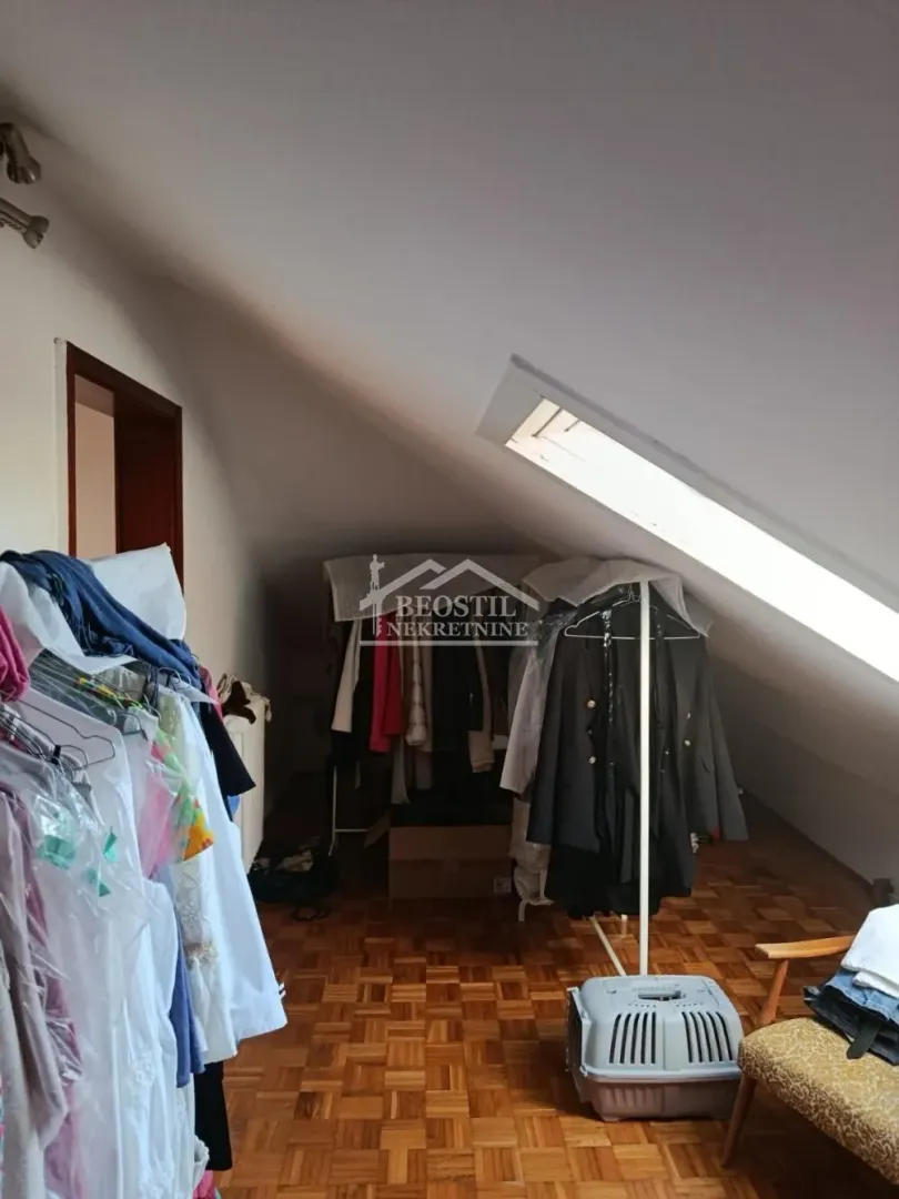 Potkrovlje sa kosim plafonom, krovnim prozorom i garderoberima sa odećom.