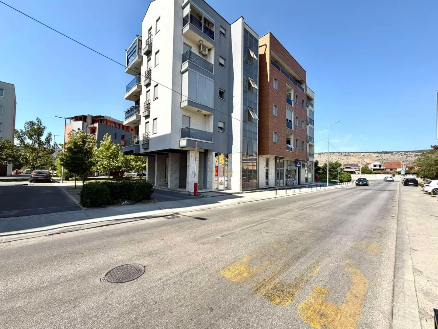 Exterior view of a modern residential building with balconies and a street in the foreground.