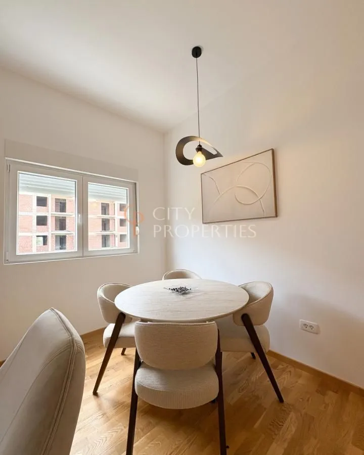 Trpezarija sa okruglim stolom, četiri stolice i modernim lusterom.