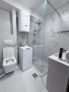 Modernly equipped bathroom with a walk-in shower, toilet, washing machine, and water heater. - image 9