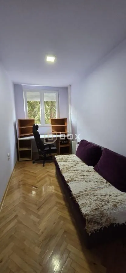Manja soba sa kaučem, radnim stolom i parketom na podu.