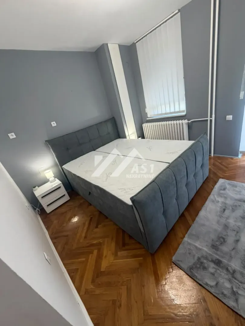 Spavaća soba sa bračnim krevetom i parketom na podu.