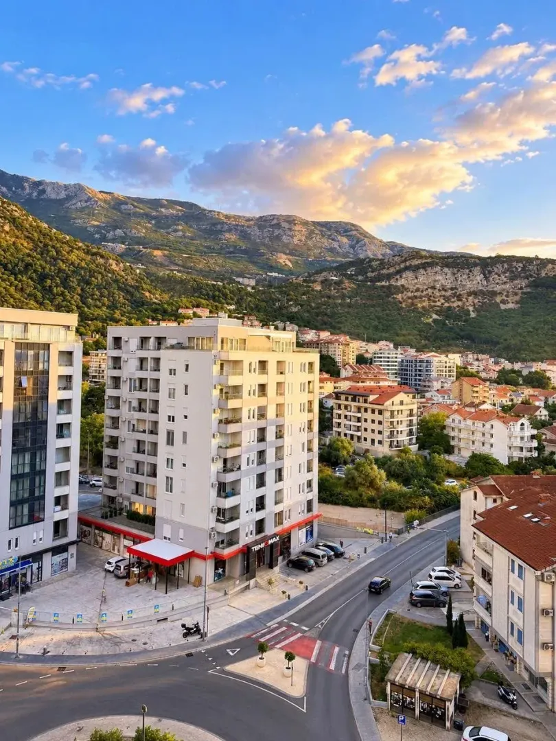 Pogled sa prozora na gradsko naselje i planine u pozadini.