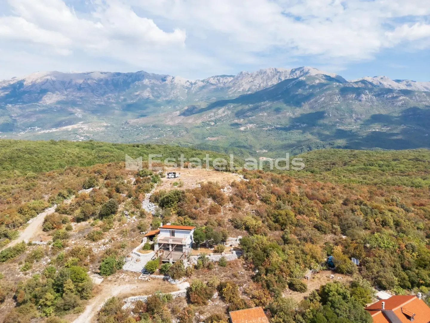 Pogled iz vazduha na kuću okruženu prirodom i planinama.