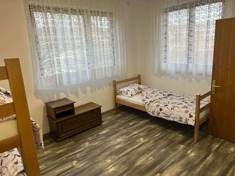 Furnished bedroom with wooden beds and two windows with white curtains.