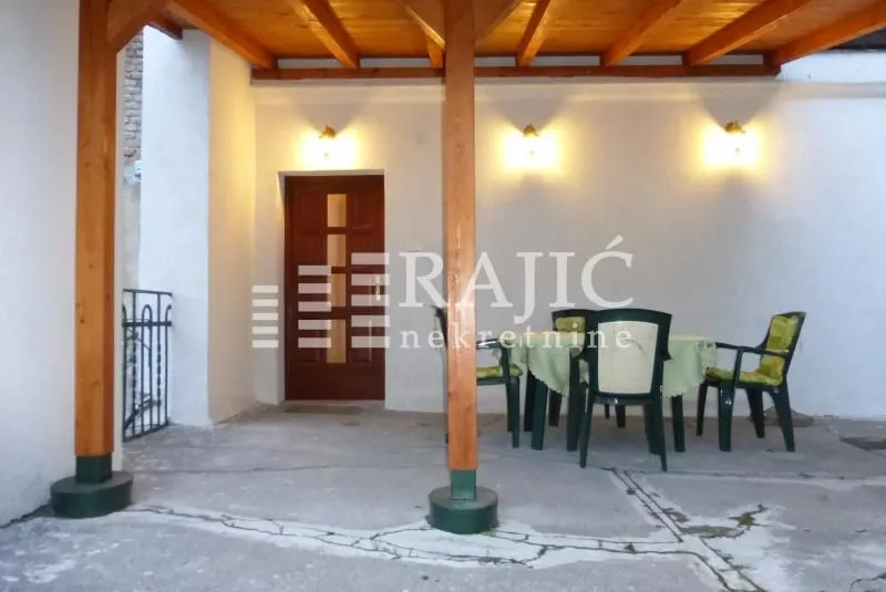 Natkrivena terasa ispred ulaza u kuću sa garniturom za sedenje.