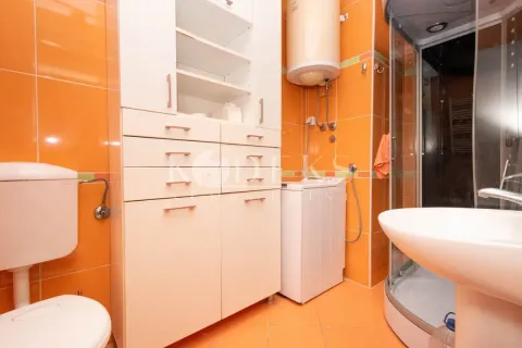 Bathroom with orange tiles, shower cabin, washbasin, and white cabinet. - image 7
