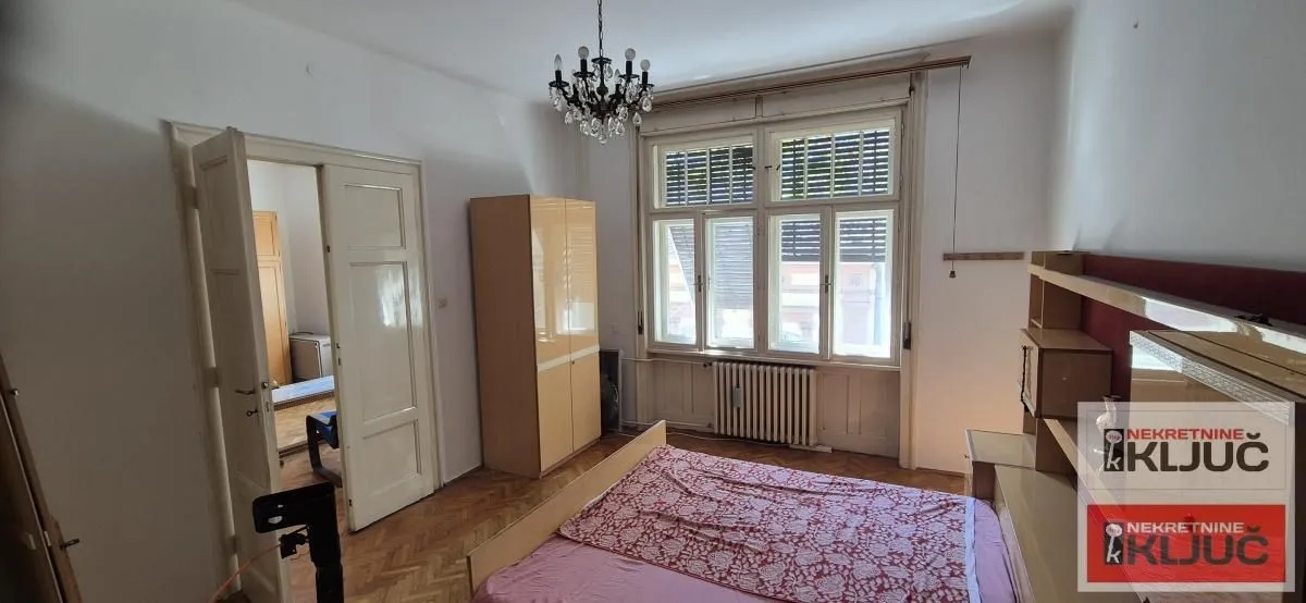 Nameštena spavaća soba sa velikim prozorima i drvenim podom.