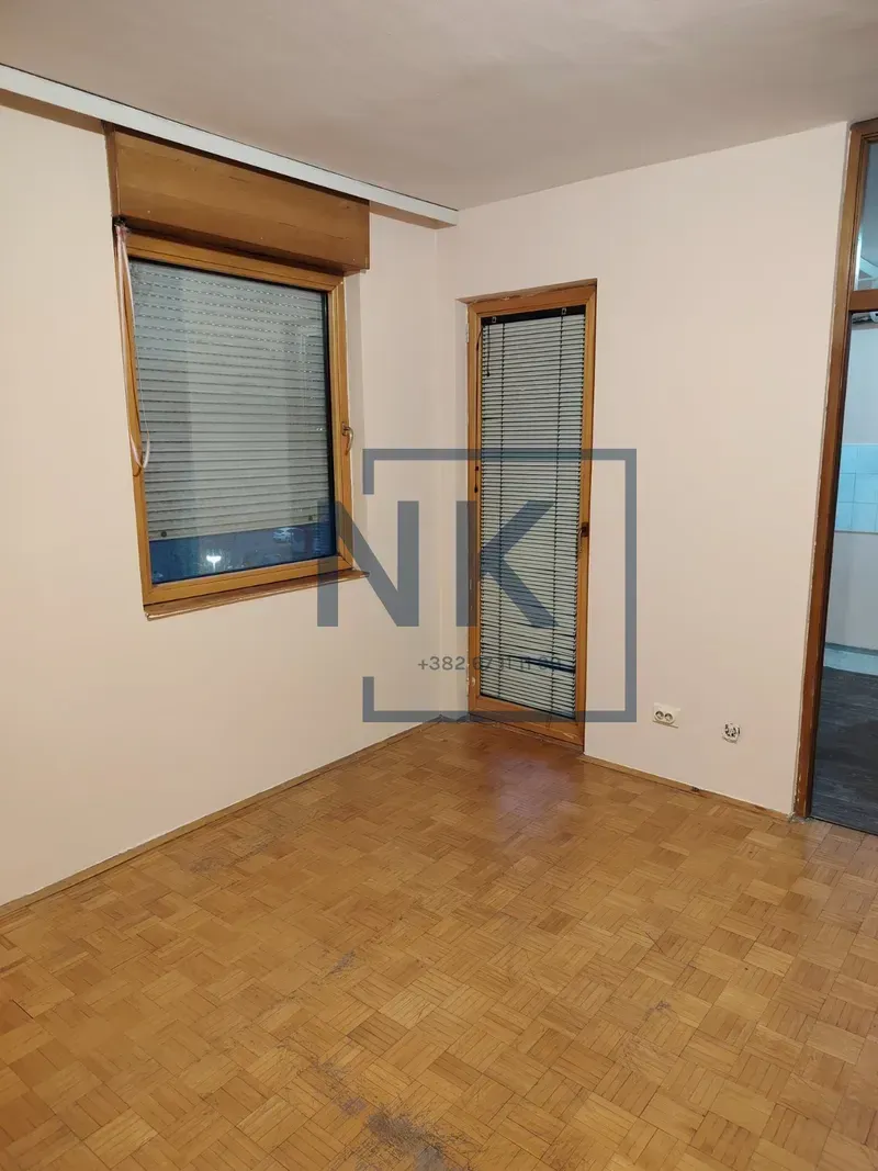 Empty room with wooden parquet flooring and a window with blinds.
