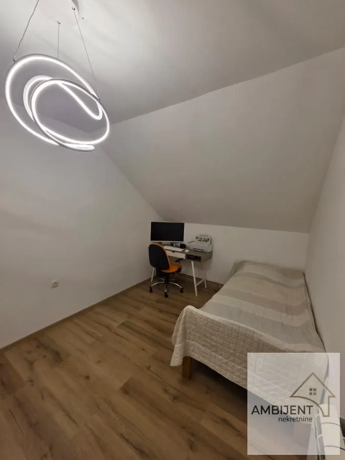 Small bedroom with a bed, desk, and modern chandelier under a sloped ceiling.