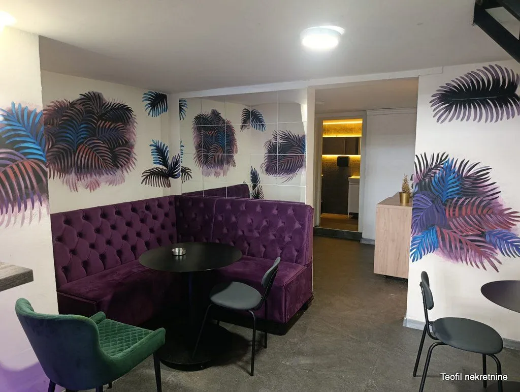 Living room with a purple corner sofa, a black table, and painted walls with leaf motifs.